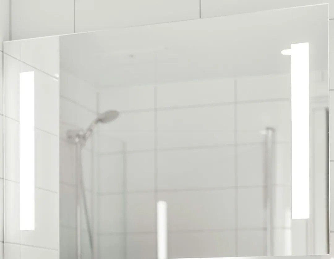 Lighted bathroom mirror above a white tile wall and a chrome faucet in a renovated Manhattan bathroom
