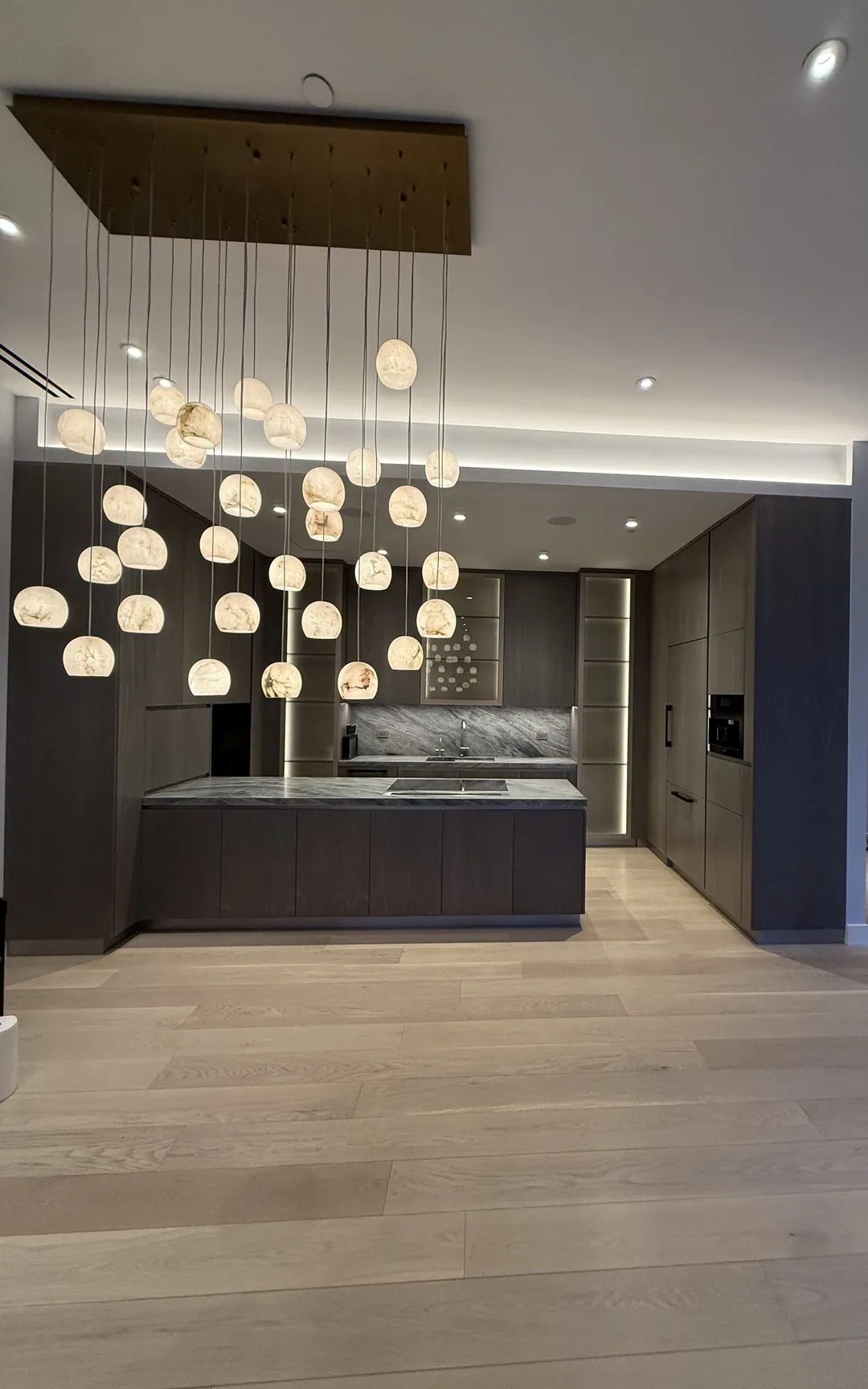 Contemporary Manhattan kitchen with grey wood cabinetry, a long island and cluster pendant lighting